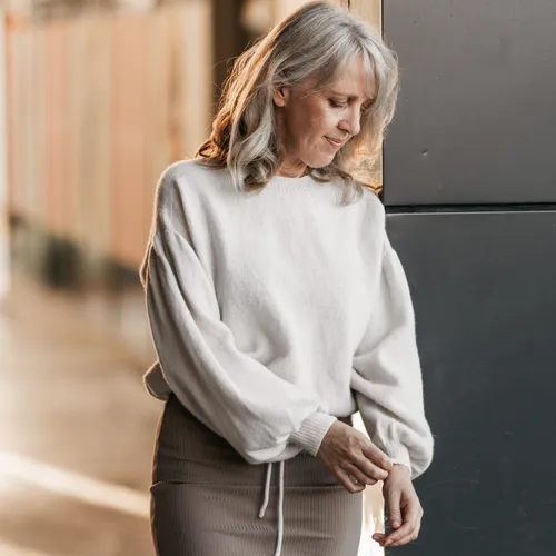 A woman looking down at the cuff on her cream coloured hand knit sweater